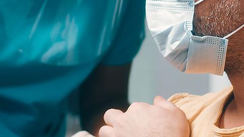 Woman in scrubs and face shield delivers vaccination to man in face mask