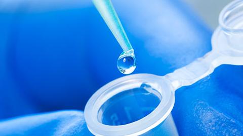 A pair of hands squeeze testing fluid from a syringe into a vial